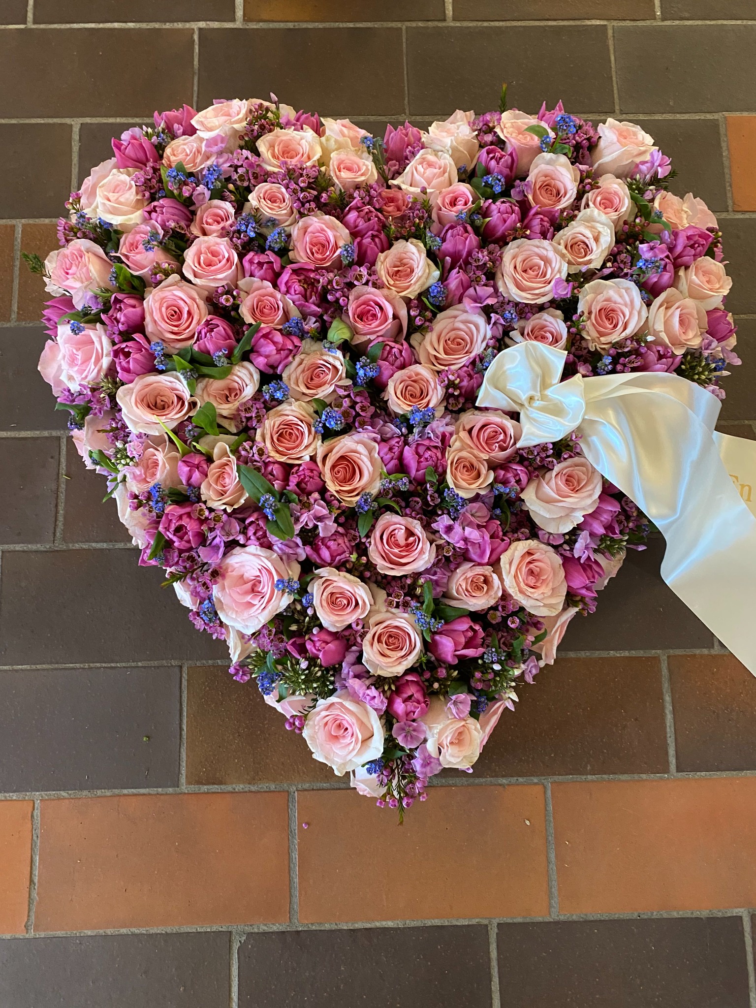 Hjerteformet blomsterdekoration med rosa og røde roser samt lyserøde blomster.