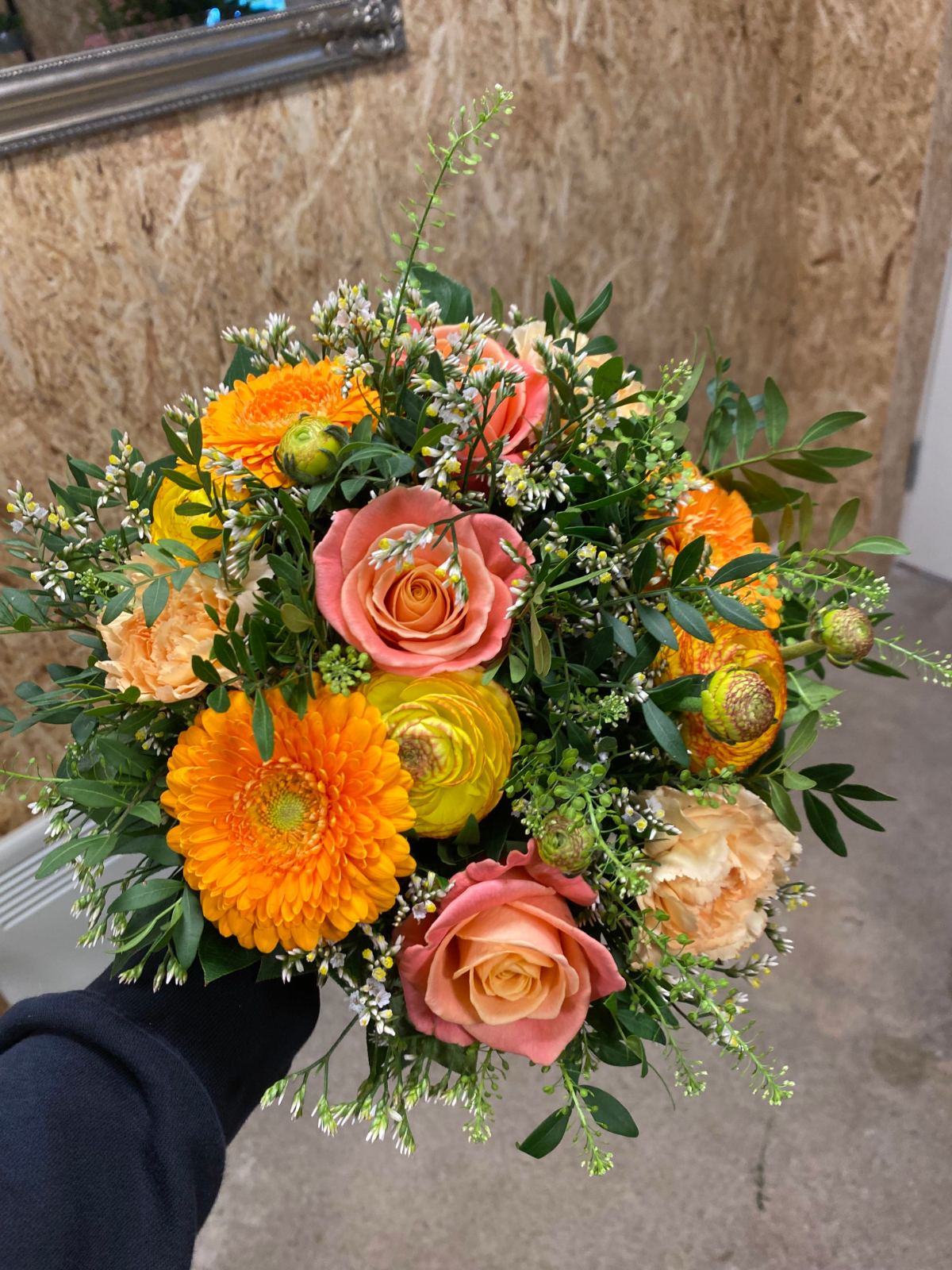 Håndbundet buket med orange gerbera, rosa roser og sæsonens grønt.
