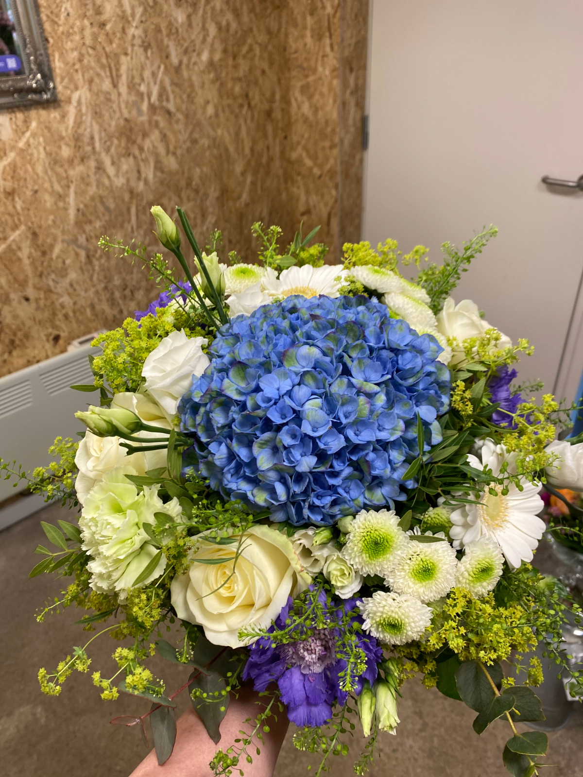 Buket med blå hortensia, hvide roser og grønne nuancer.