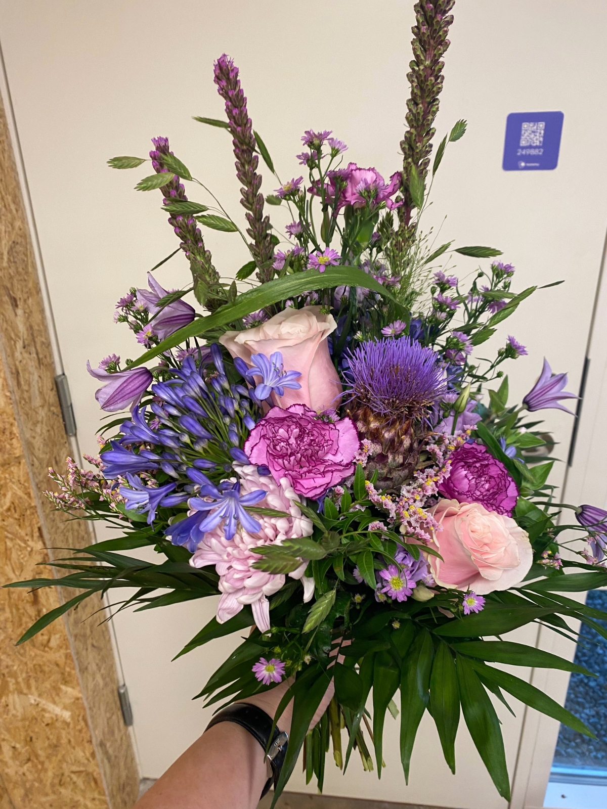 Luftig buket med lilla og rosa blomster samt dekorativt grønt.