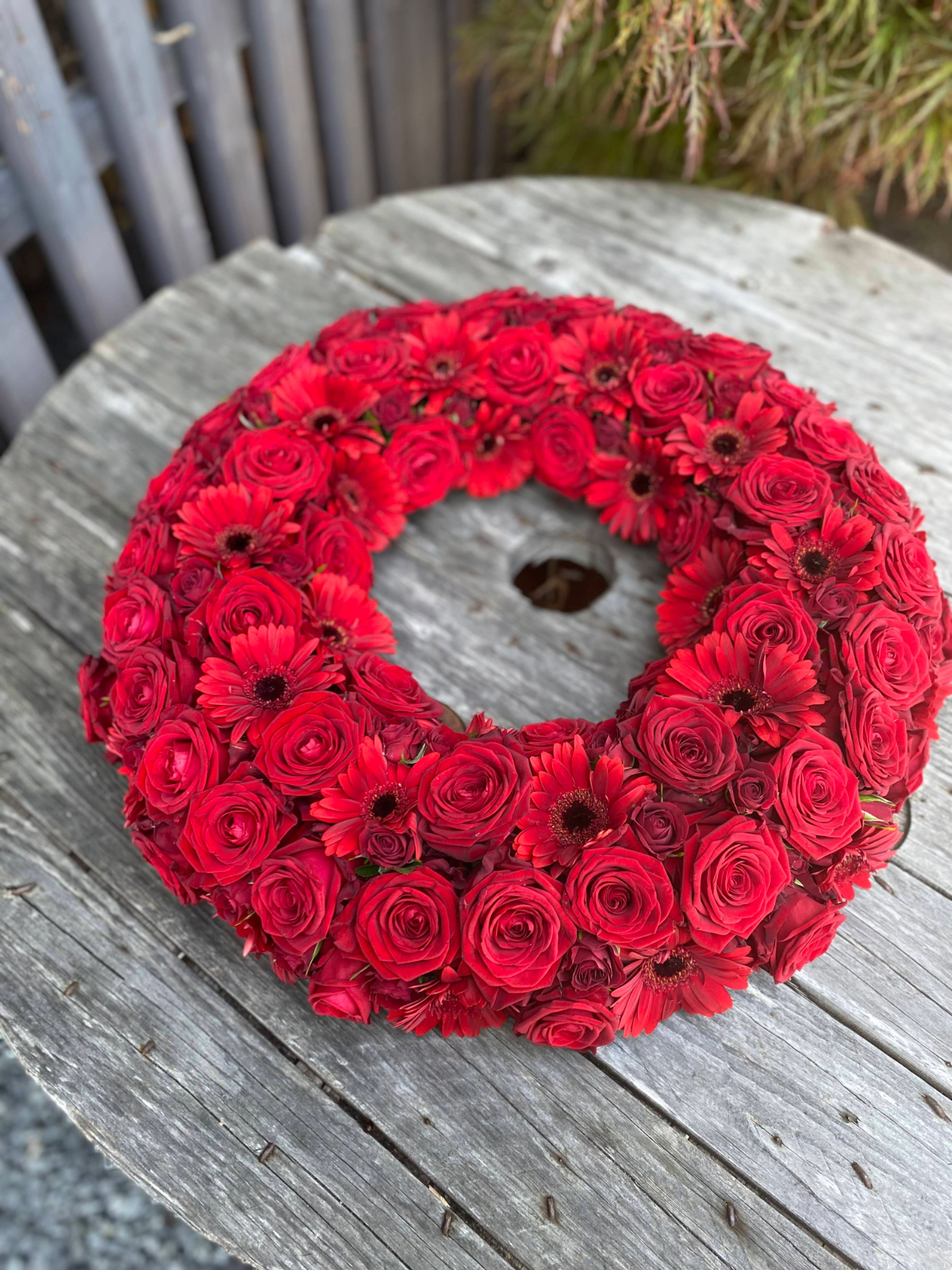 Rød blomsterkrans tæt bundet med roser og gerbera.