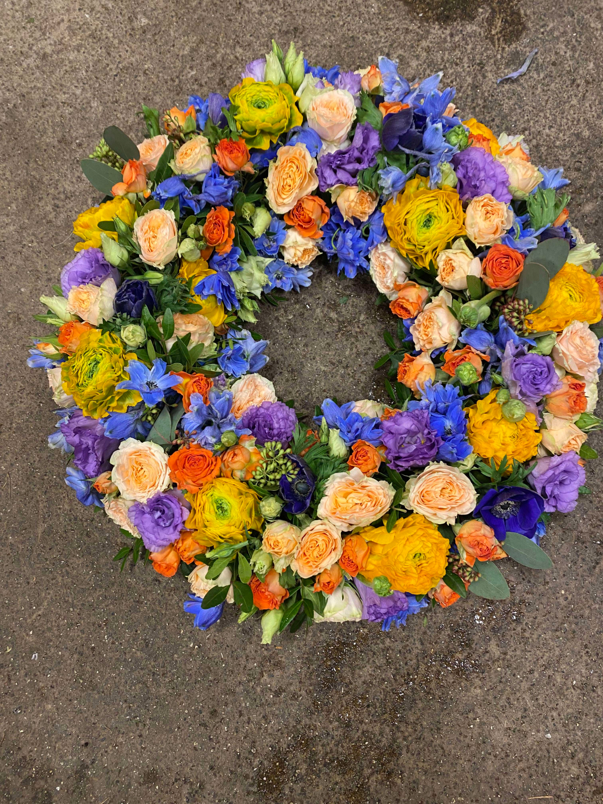 Farverig blomsterkrans med gule, orange, blå og lilla blomster.