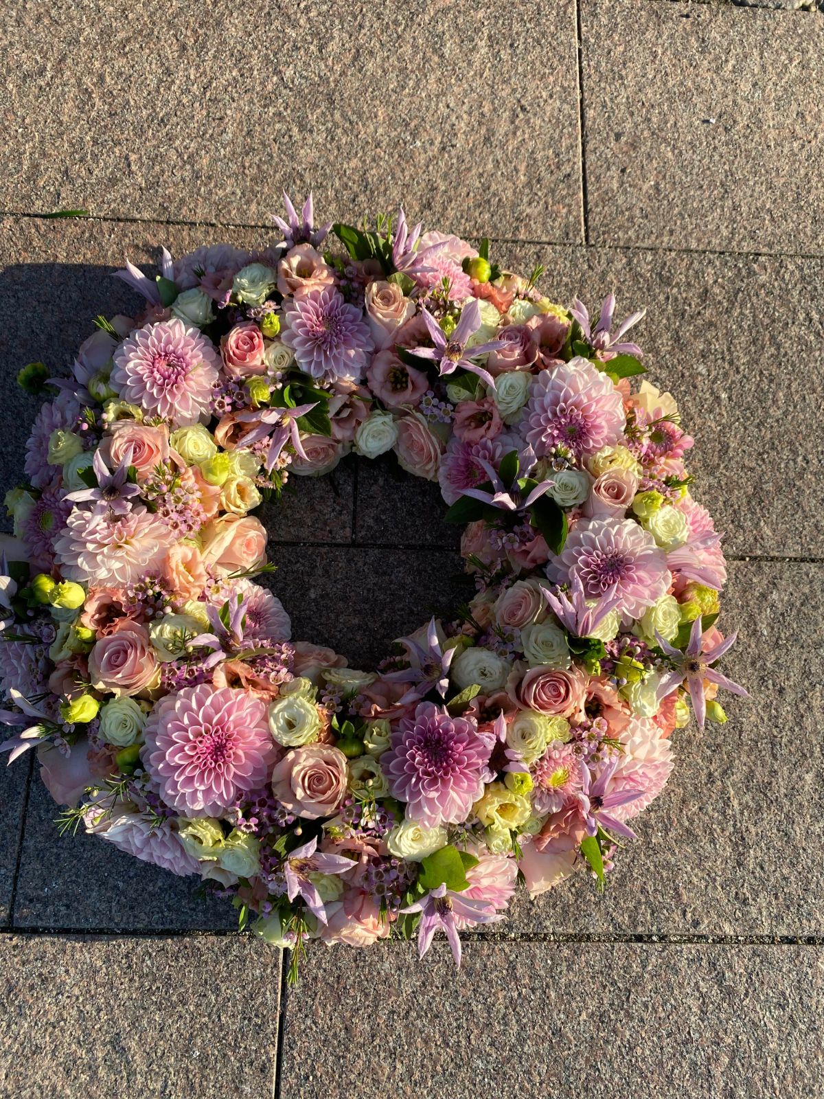 Pastelfarvet blomsterkrans med rosa georginer, roser og lilla blomster.