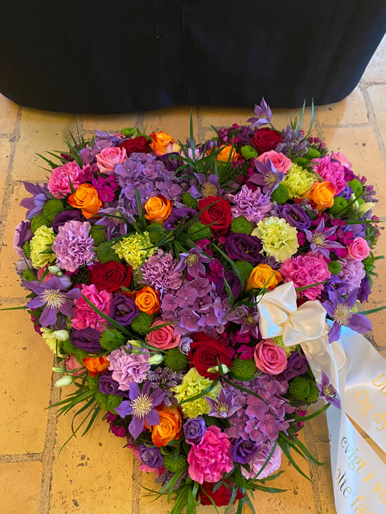Farverigt blomsterhjerte med lilla, rosa, orange og gule blomster.