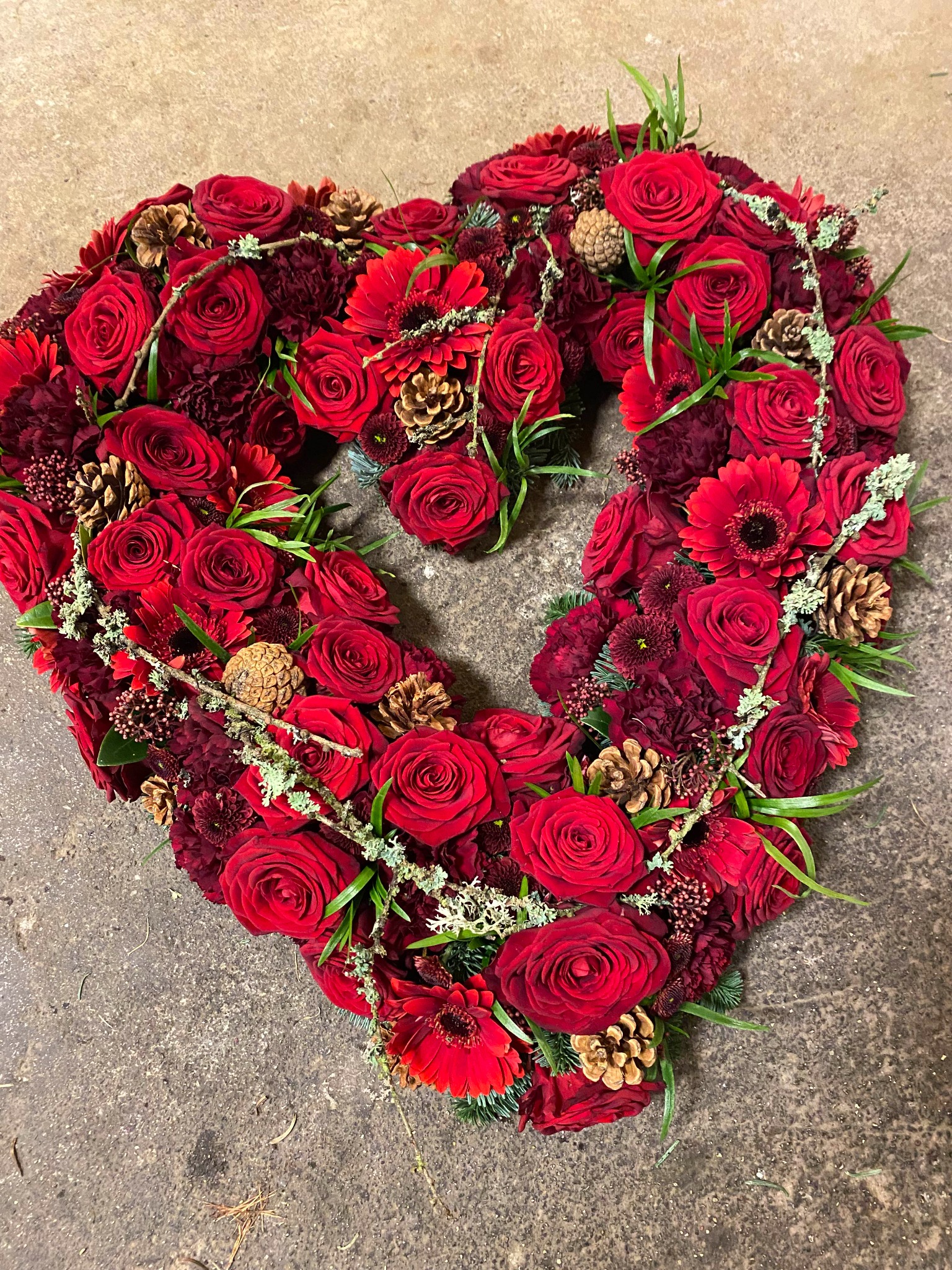 Åbent blomsterhjerte med røde roser, gerbera og dekorativt grønt.