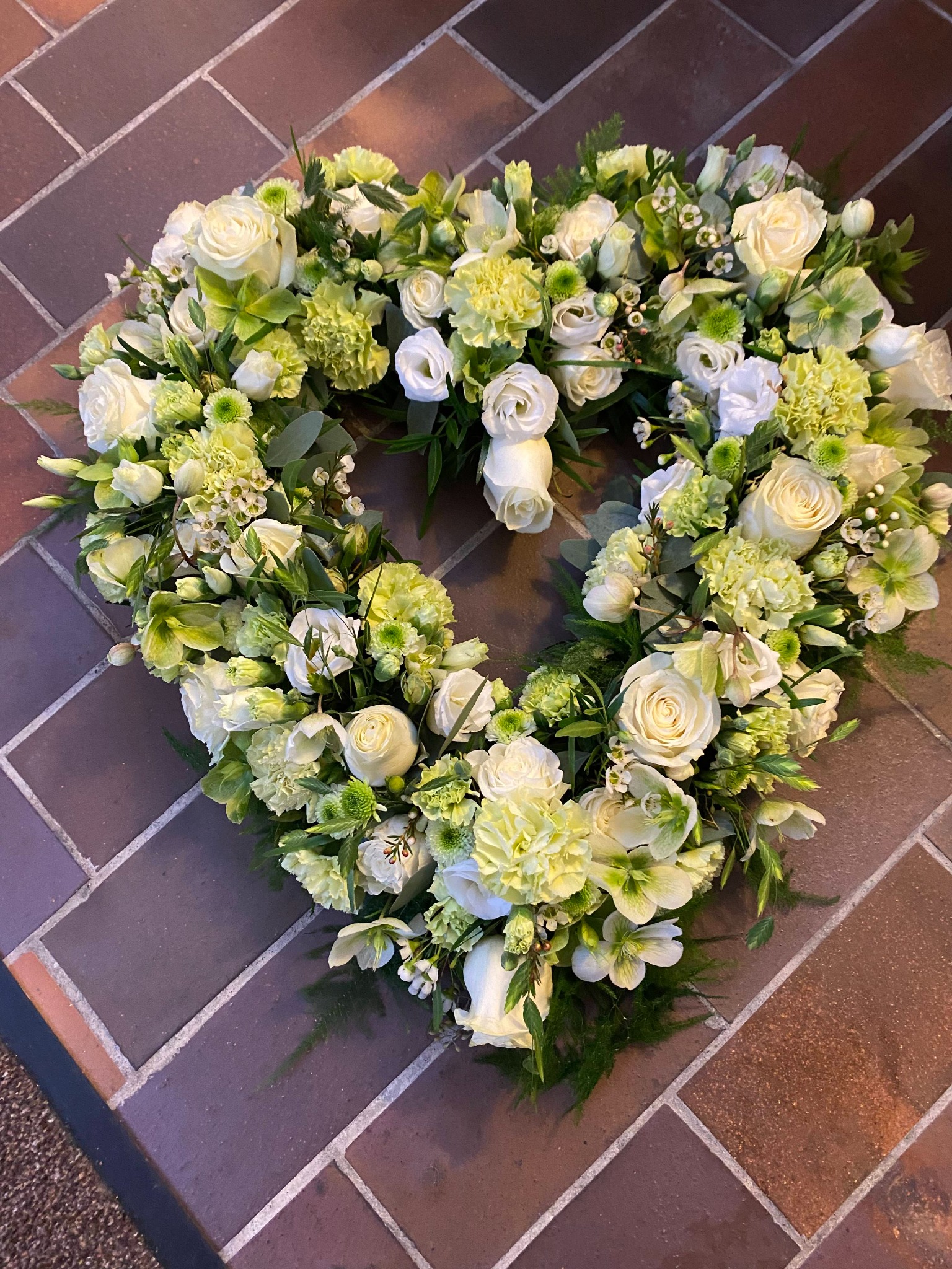 Åbent blomsterhjerte med hvide roser, lyse blomster og grønt.