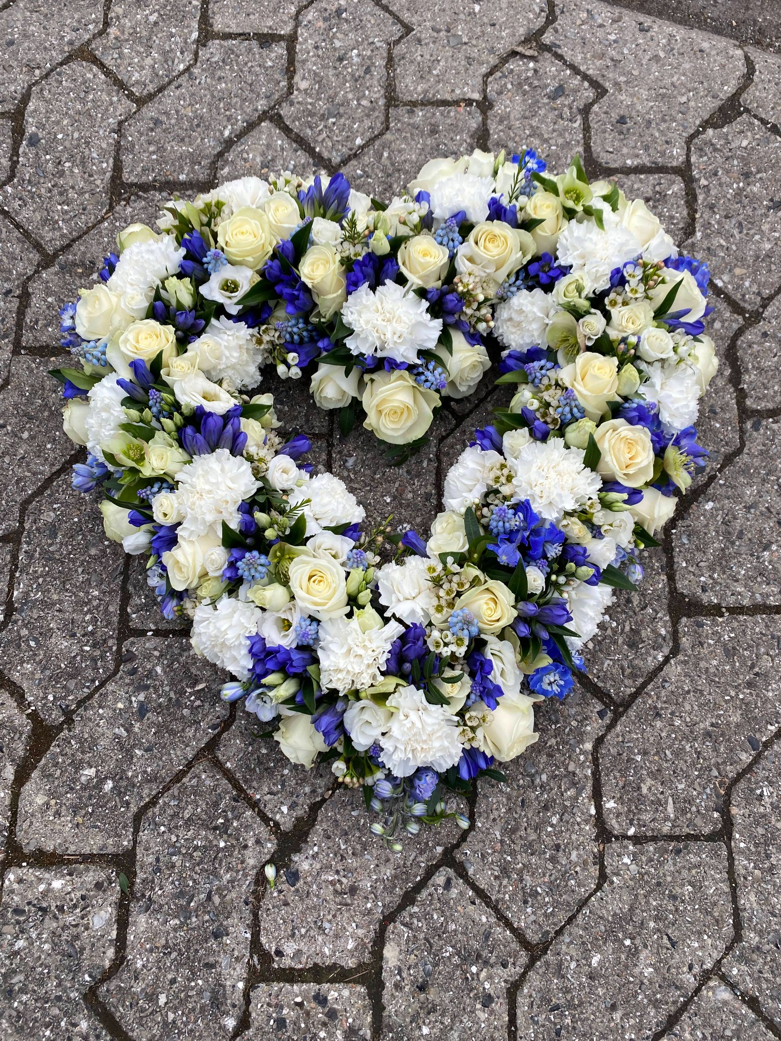 Blomsterhjerte med hvide roser og blå og lilla blomster.