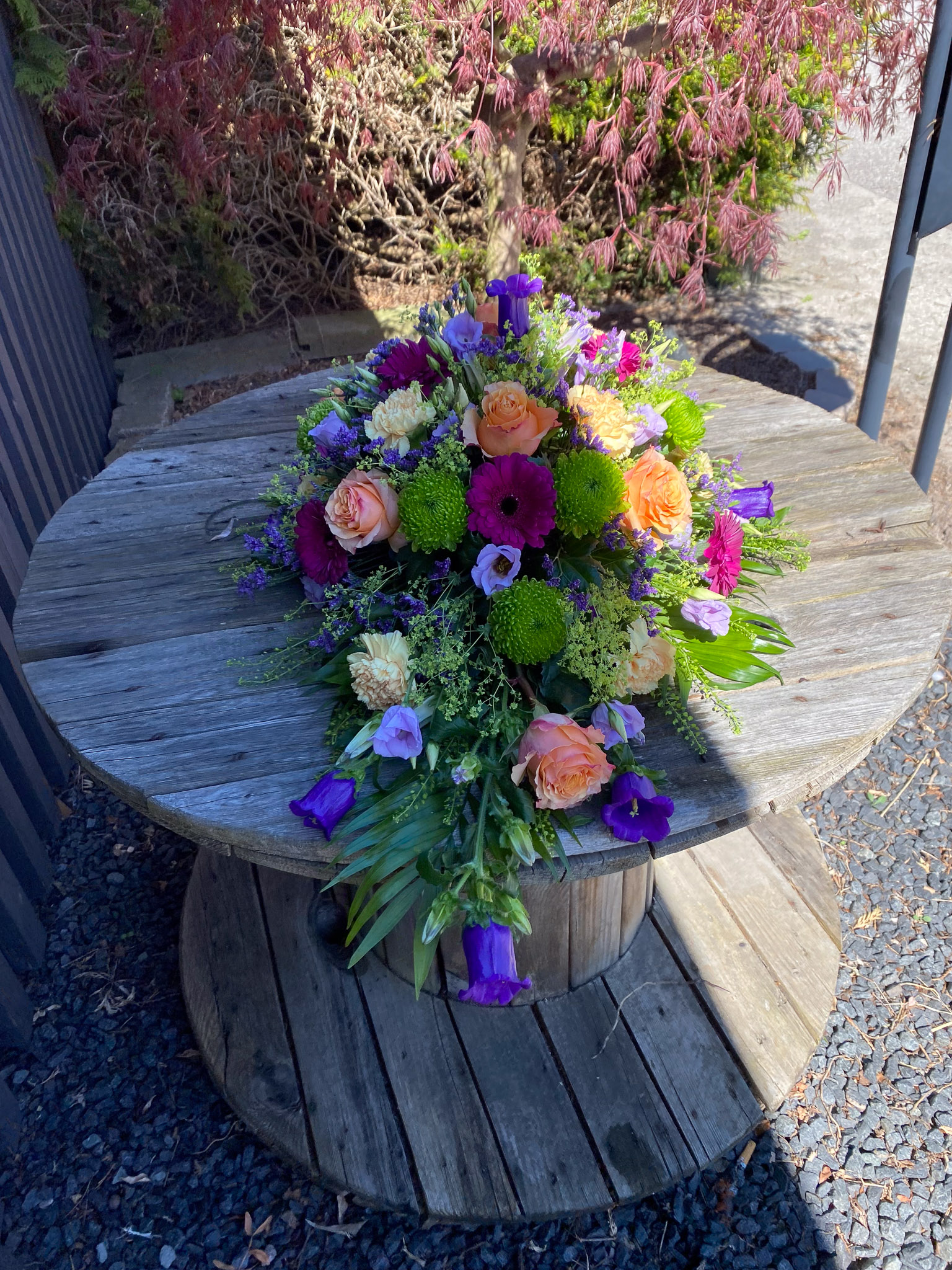 Båredekoration i lilla, pink og fersken med roser, gerbera, nelliker og klokkeblomster