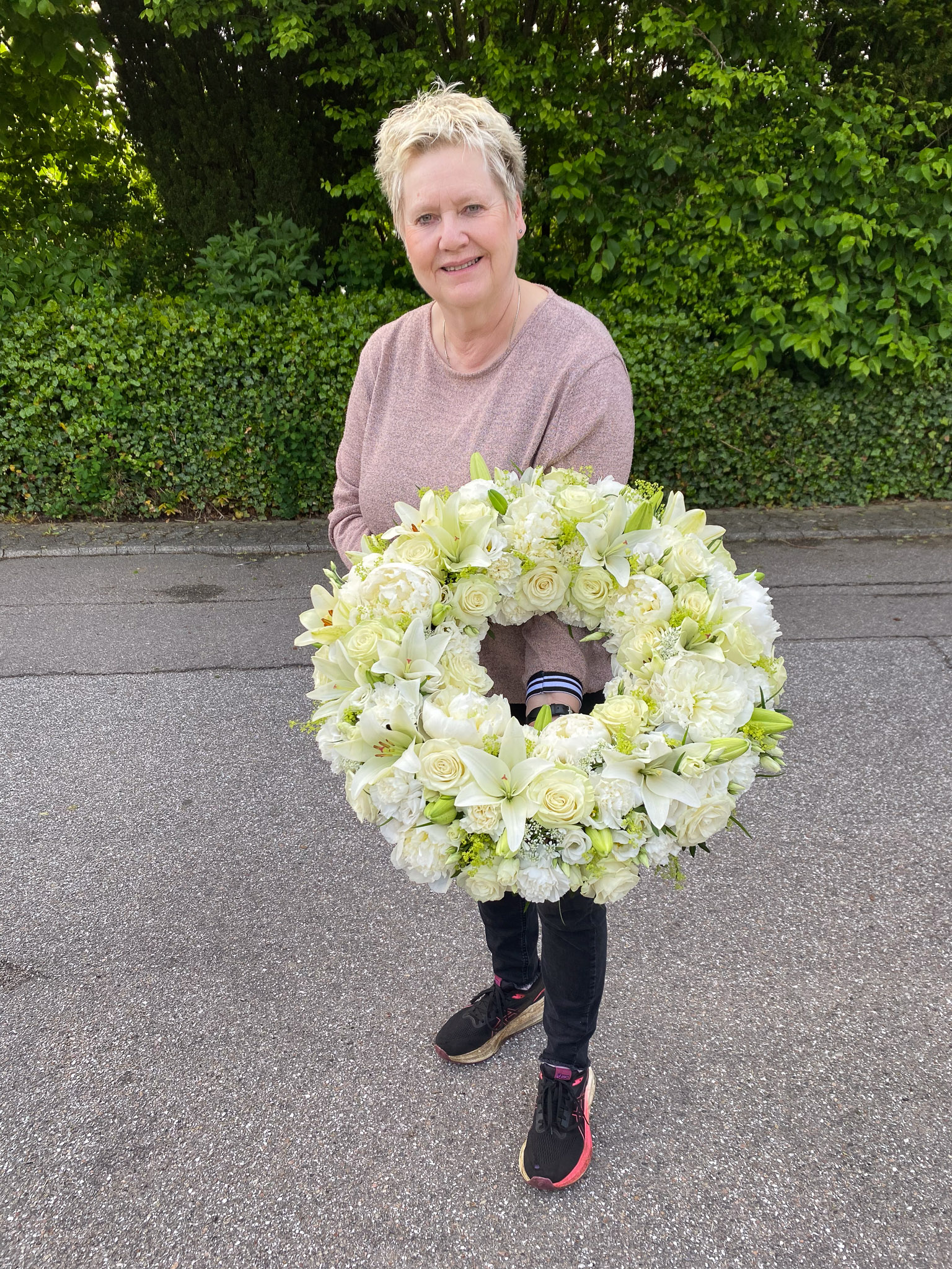 Hvid og cremefarvet krans holdt af blomsterhandler