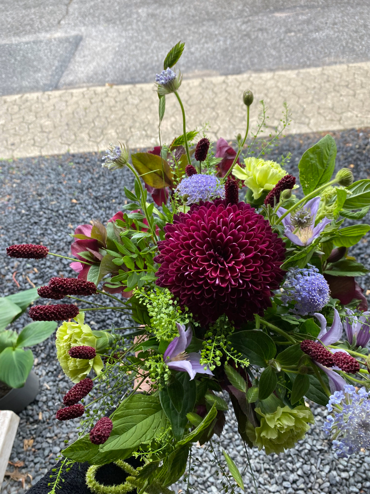Karakterfuld buket med mørkerøde blomster og hængende grønt.