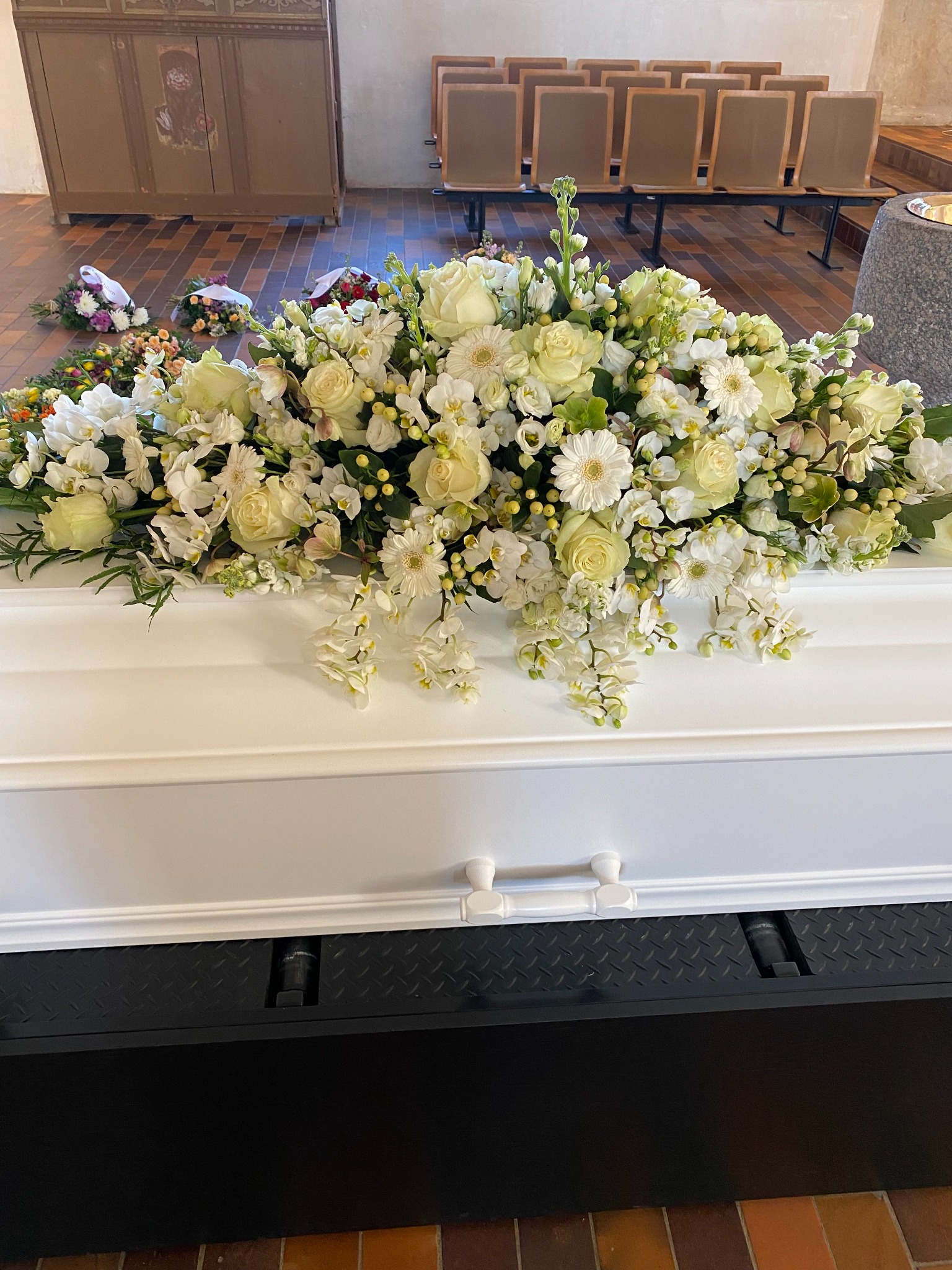 Bred kistedekoration med hvide blomster og grønne grene